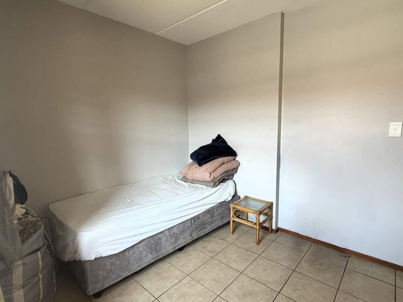 A simple bedroom featuring neutral wall paint and tiled flooring, providing a functional space with direct access to an adjoining bathroom.