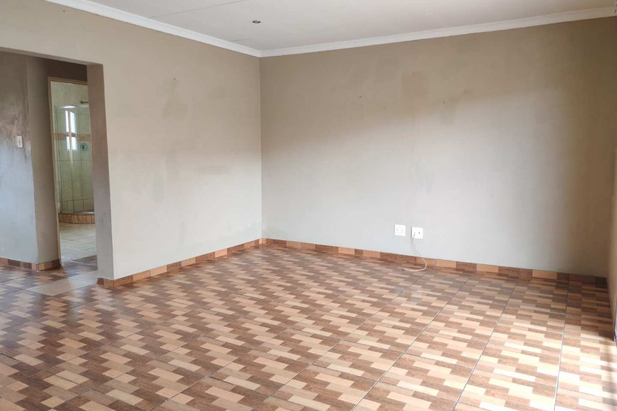 An empty living room featuring tiled flooring, recessed downlights, and neutral wall finishes, with an adjacent view into a bathroom area.