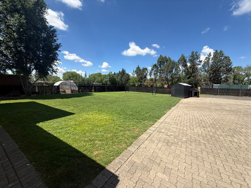 Spacious backyard featuring a well-maintained lawn, paved driveway area, and perimeter fencing, providing ample outdoor space.