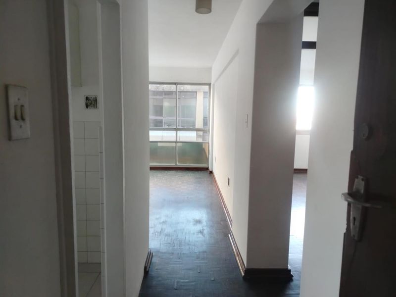 A vacant hallway featuring dark parquet flooring and access to adjacent rooms, leading towards a windowed area with natural light.
