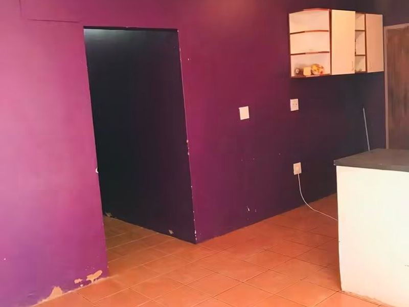 An empty kitchen space featuring tiled flooring, built-in wall cabinetry, and a kitchen island, requiring cosmetic updates to the wall finishes.