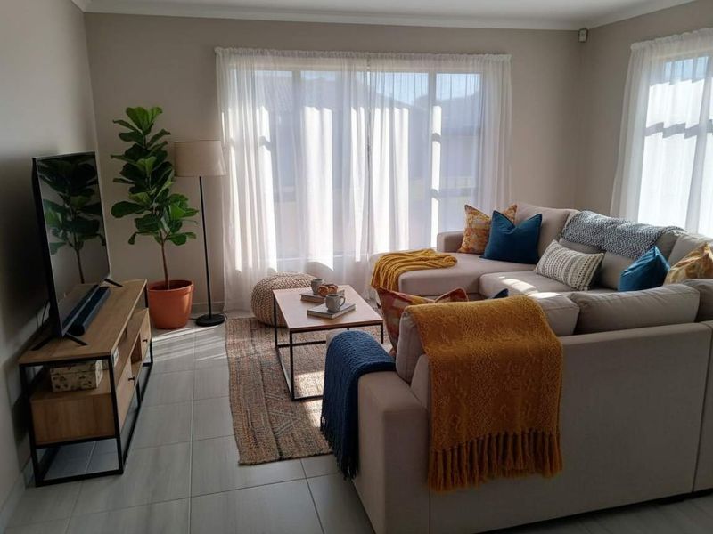 A bright and well-maintained living room featuring neutral wall tones, large windows with natural light, and modern tiled flooring.