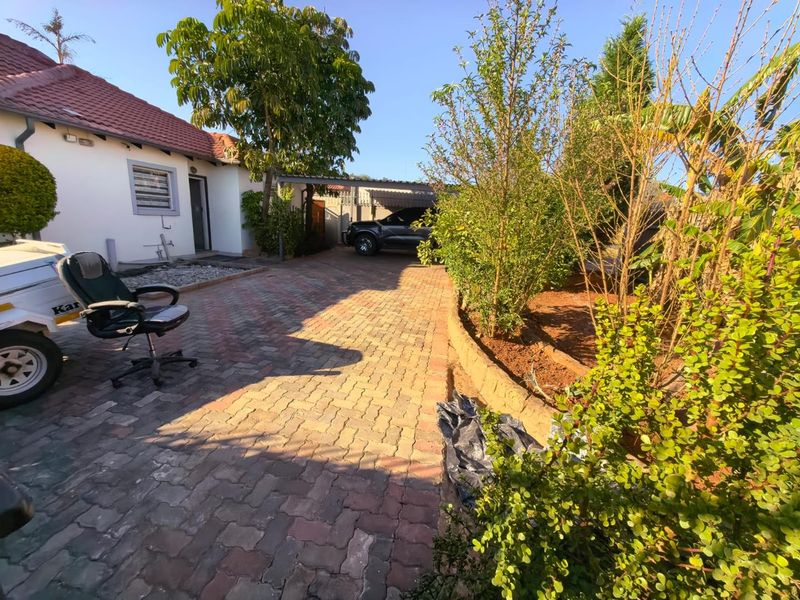 Front exterior view of the property featuring a paved driveway, carport, and landscaped garden area with a retaining wall.