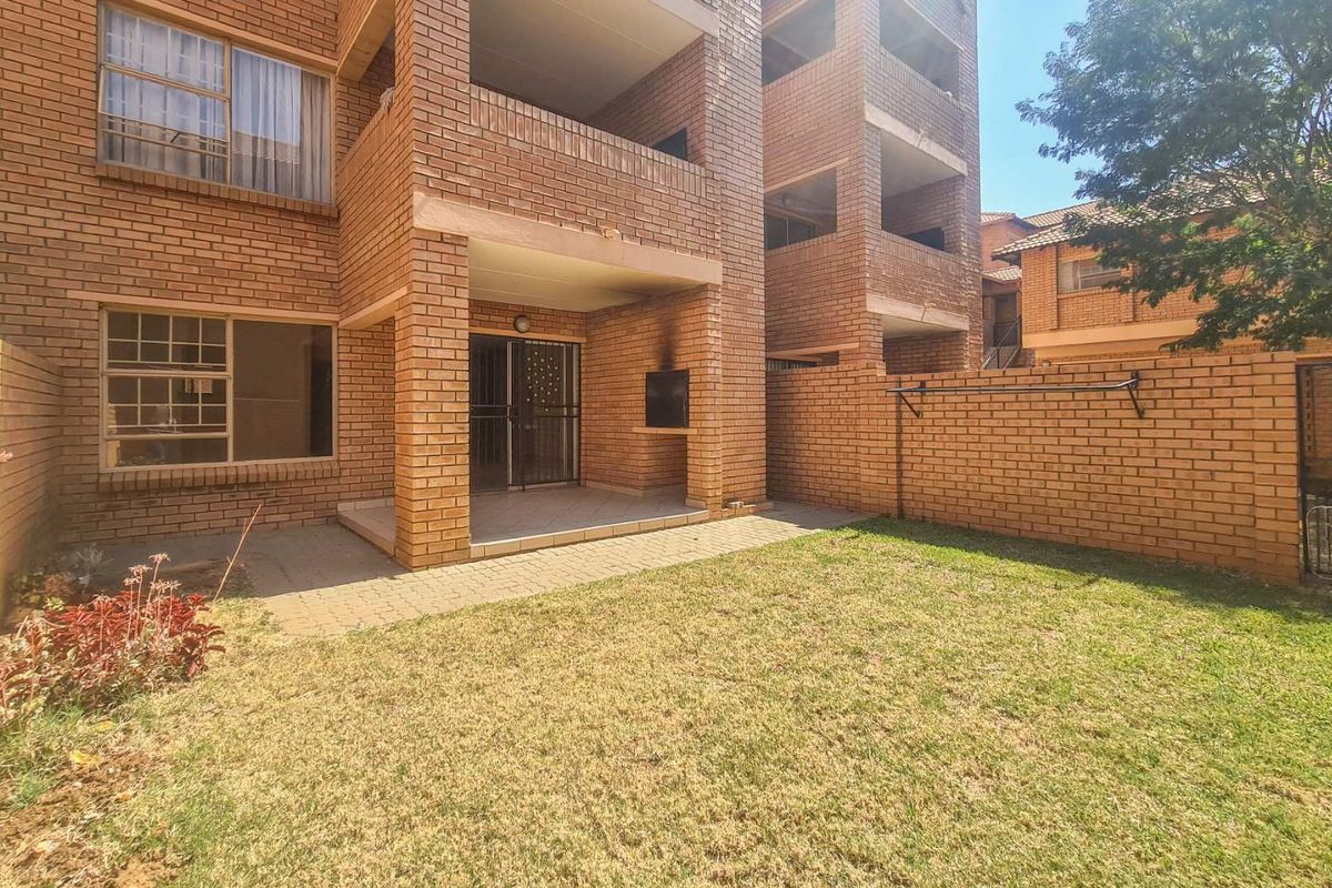 Rear view of the apartment featuring a private garden, covered patio with a built-in braai, and brick boundary wall.
