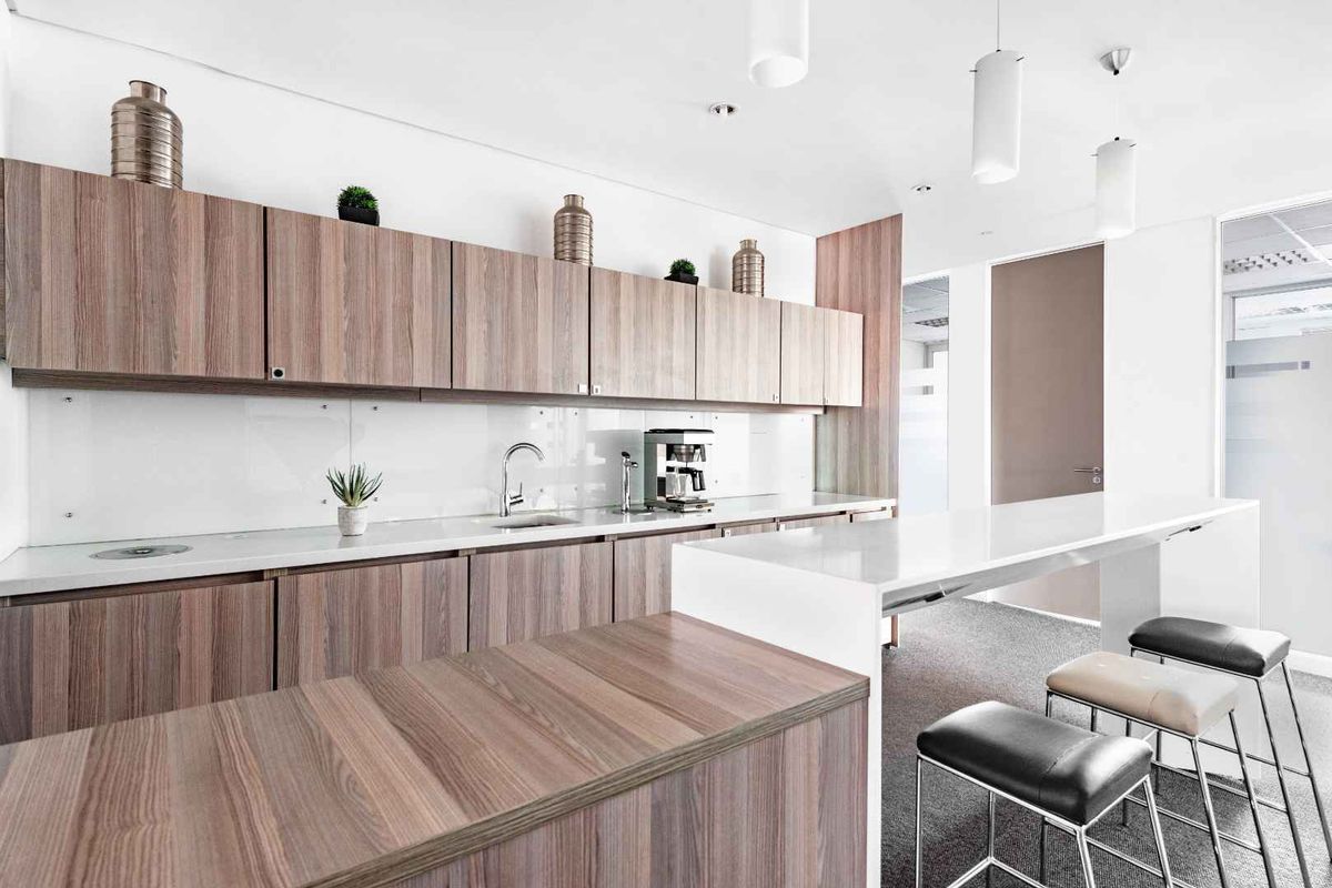 Modern office kitchenette featuring wood-grain cabinetry, white stone countertops, integrated sink, and a sleek breakfast bar area.