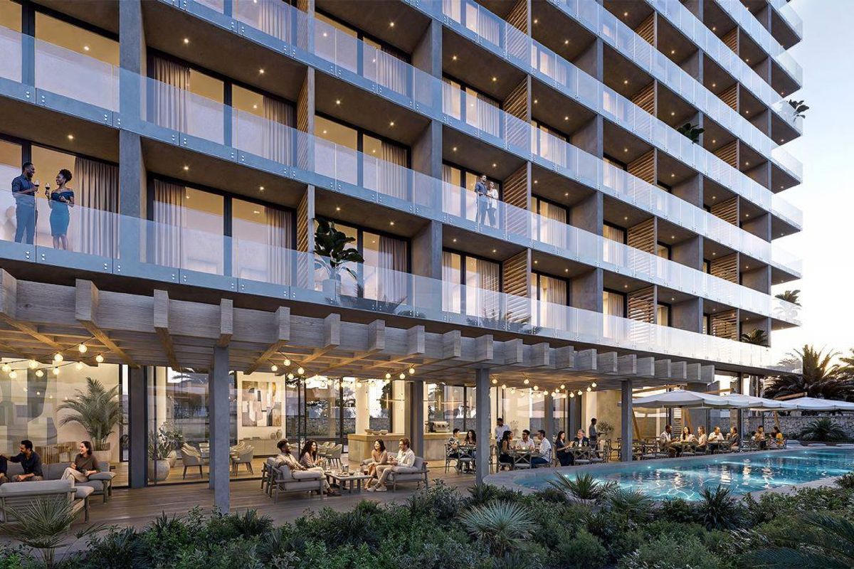 A modern apartment building exterior featuring a ground-level pool area, covered patio, and glass-railed balconies on upper floors.