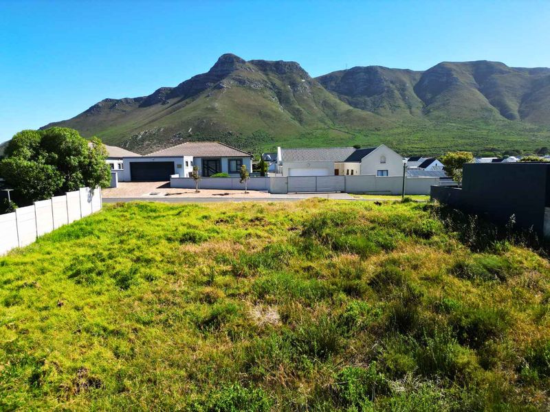 A vacant residential plot of land featuring mountain views, situated in a developed neighborhood with established boundary walls.