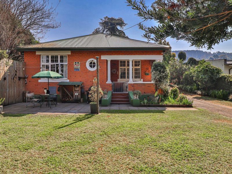 A charming single-story brick home featuring a covered porch, paved patio area, and a spacious garden setting.