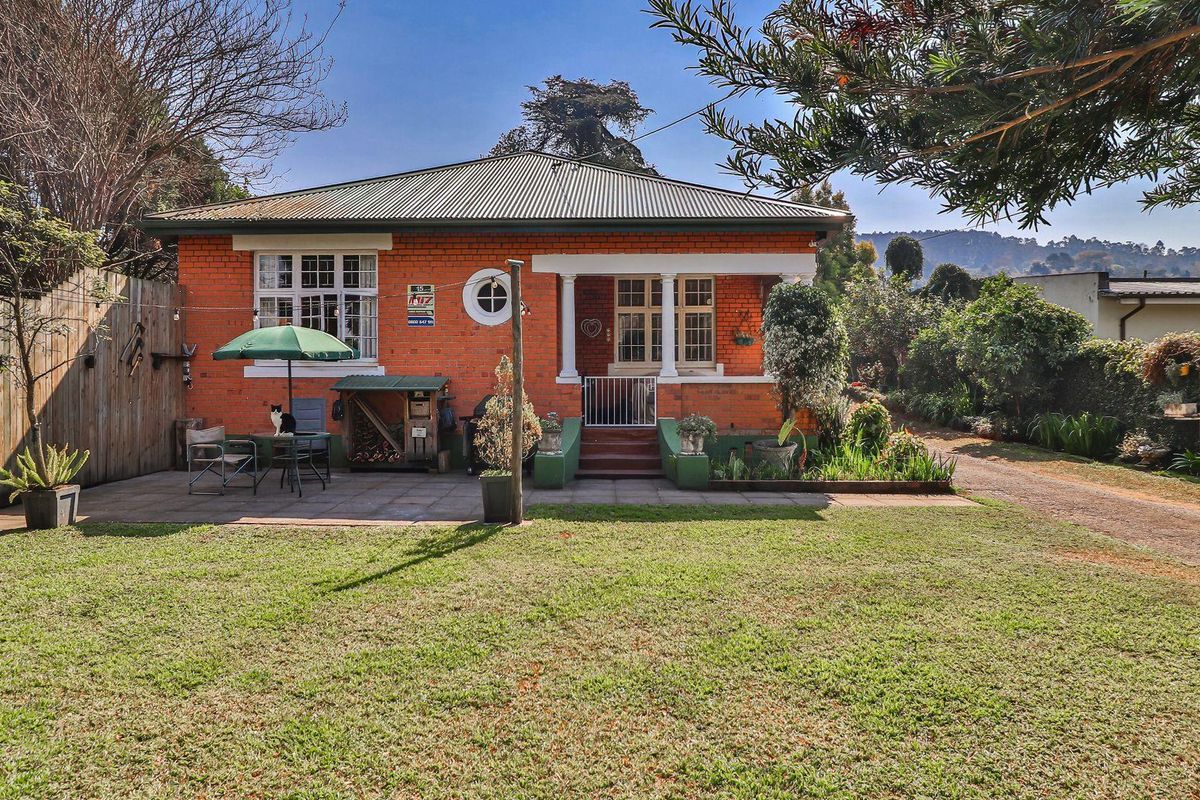 A charming single-story brick home featuring a covered porch, paved patio area, and a spacious garden setting.