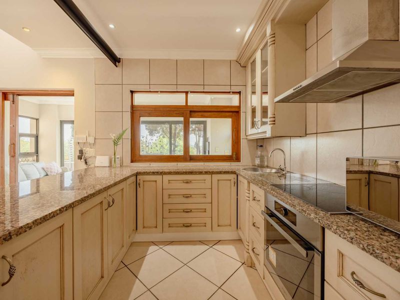 A well-appointed kitchen featuring granite countertops, built-in oven, electric hob, extractor fan, and tiled backsplash with ample cabinetry and natural light.