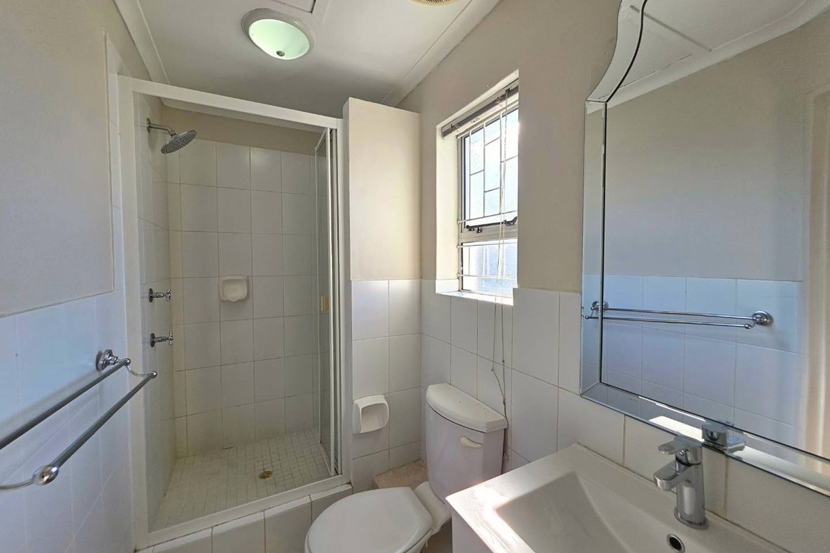 A functional bathroom featuring a shower enclosure, toilet, and vanity basin with a wall-mounted mirror.