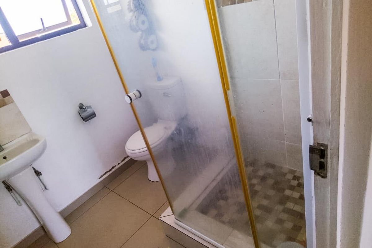 A functional bathroom featuring a pedestal basin, toilet, and a glass-enclosed shower with tiled finishes.