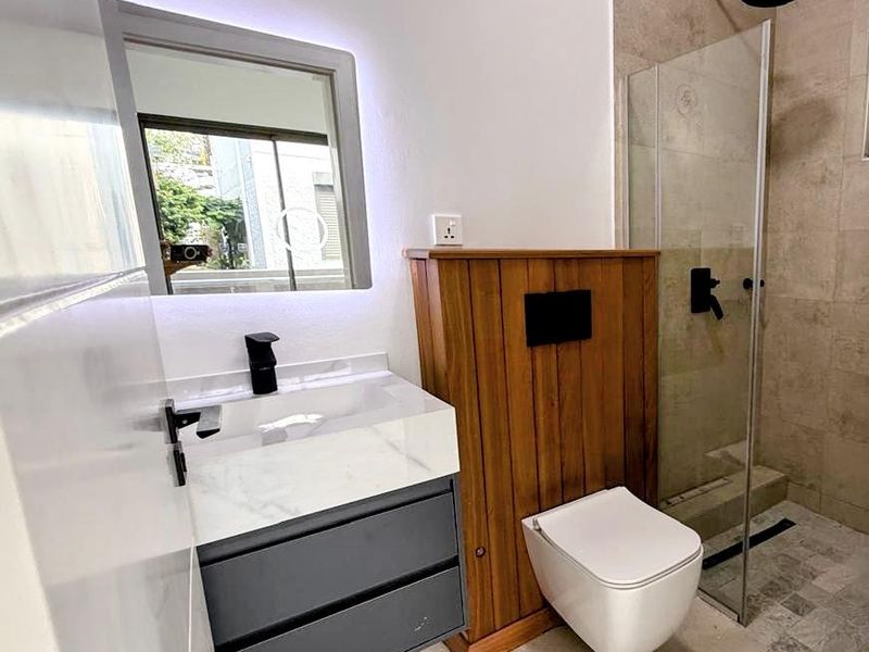 Modern bathroom featuring a wall-mounted toilet with wood-panelled cistern, marble-topped vanity with integrated basin, and a glass-enclosed walk-in shower with rainfall showerhead.