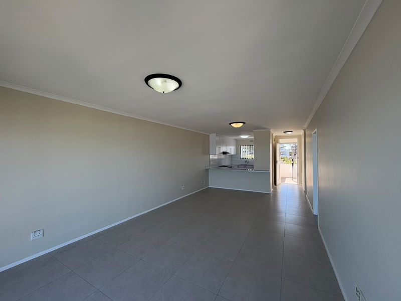 Spacious open-plan living area featuring tiled flooring and a functional kitchen with built-in cabinetry, leading to an exterior balcony entrance.
