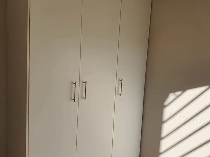 A bright bedroom featuring a modern white built-in wardrobe and neutral tiled flooring, offering a clean and functional storage solution.