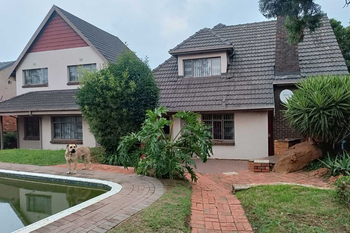 Rear view of a double-story house featuring a tiled roof, brick facade, paved patio area, and an adjacent swimming pool.
