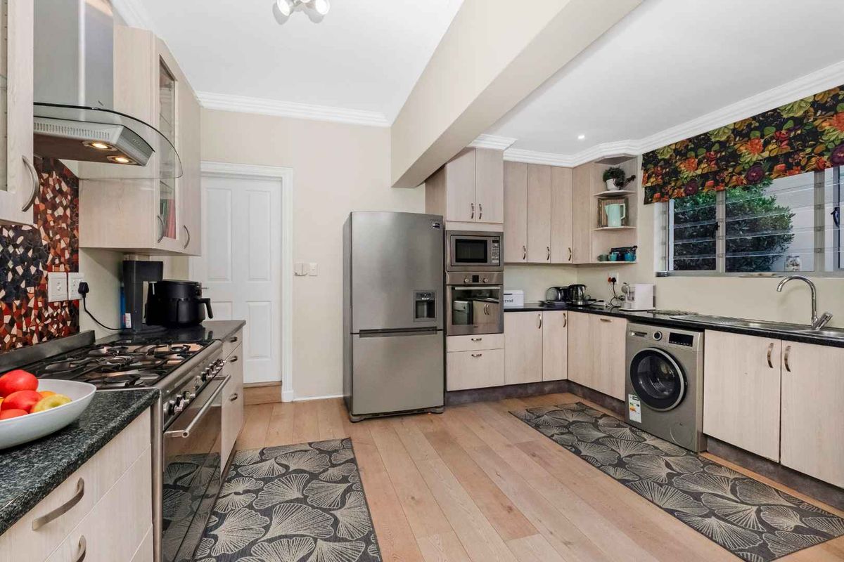 Functional kitchen featuring light wood cabinetry, granite countertops, stainless steel appliances, integrated oven, and a dedicated laundry area with washing machine connection.