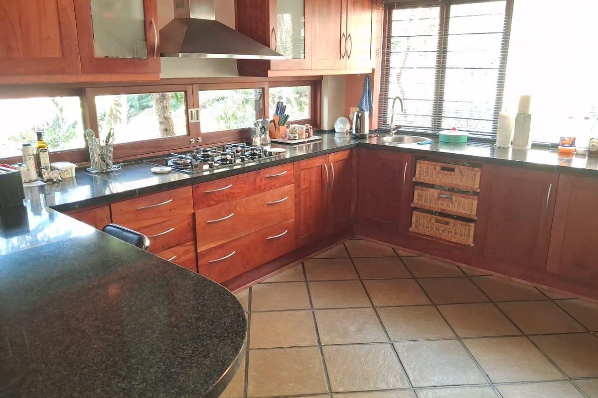 A functional kitchen featuring dark granite countertops, warm-toned wooden cabinetry, a built-in gas hob, stainless steel extractor fan, and tiled flooring.