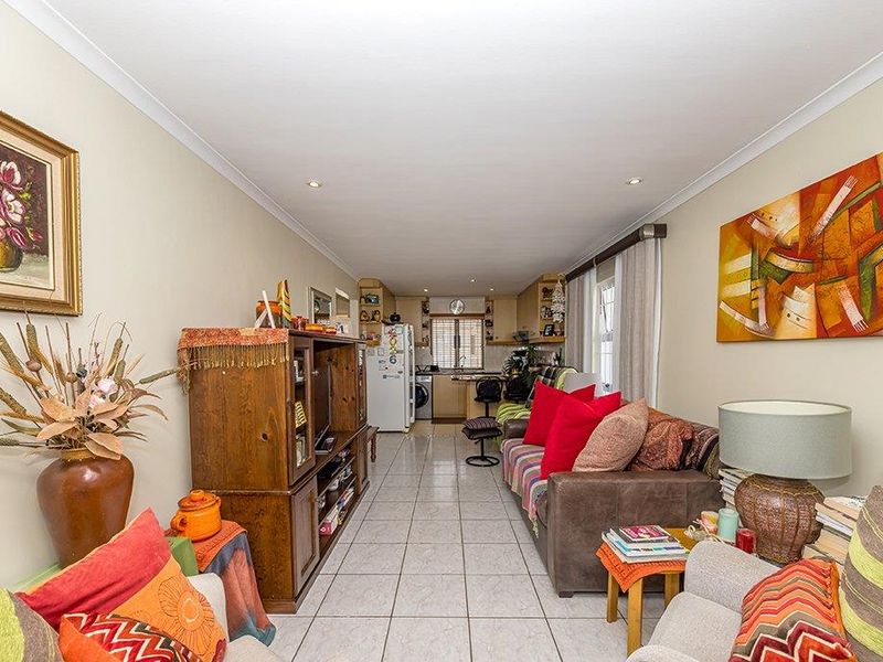 Open-plan living area featuring tiled flooring and recessed lighting, seamlessly connecting to a functional kitchen space at the rear.