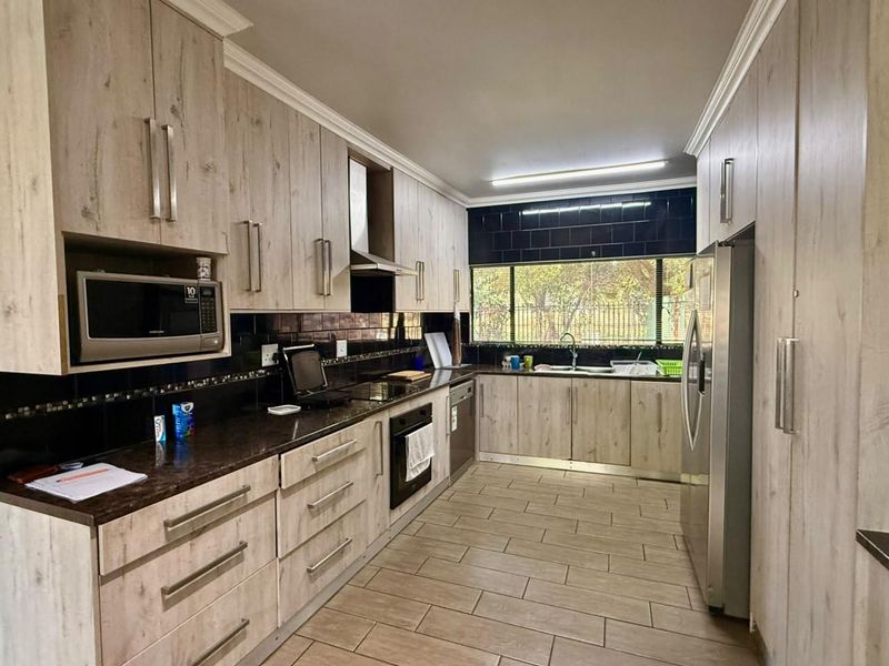 A well-maintained galley-style kitchen featuring light wood-grain cabinetry, dark granite countertops, a built-in oven, extractor fan, and a double sink with garden views.