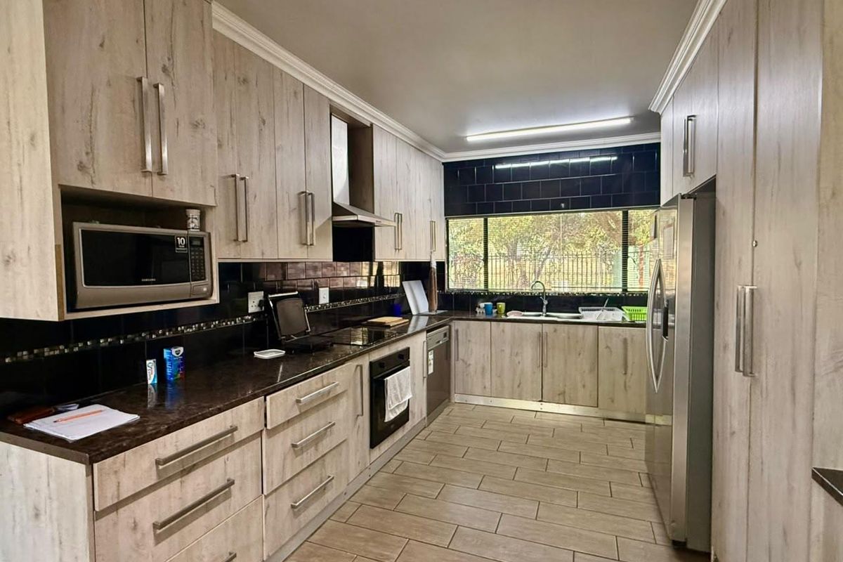 A well-maintained galley-style kitchen featuring light wood-grain cabinetry, dark granite countertops, a built-in oven, extractor fan, and a double sink with garden views.