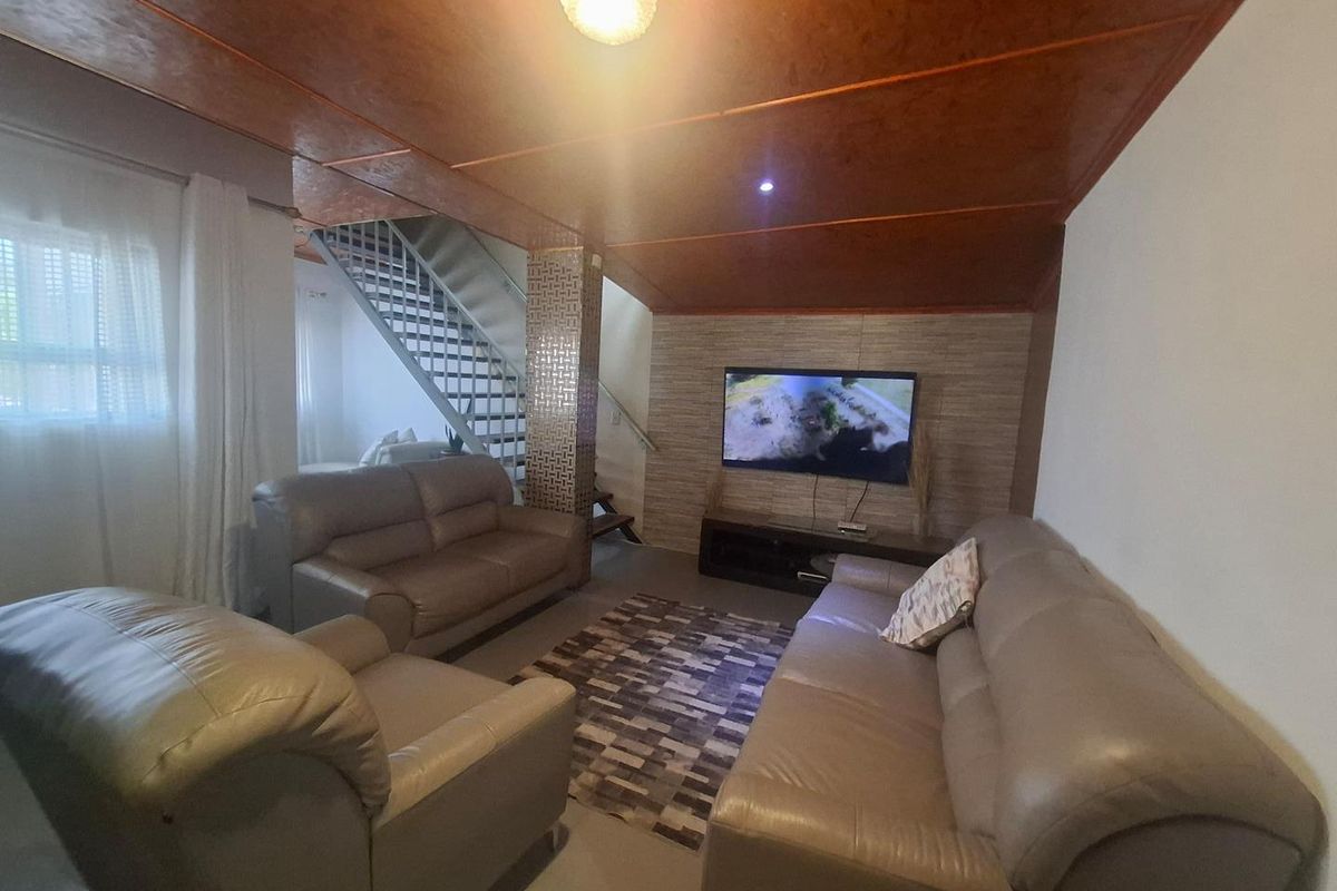 A living room featuring a staircase, textured wall cladding, and a wood-paneled ceiling, providing a functional and cozy lounge area.