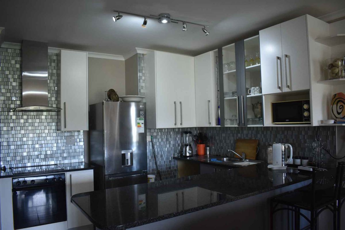 Modern kitchen featuring granite countertops, mosaic tile backsplash, stainless steel extractor fan, and ample white cabinetry with integrated storage solutions.