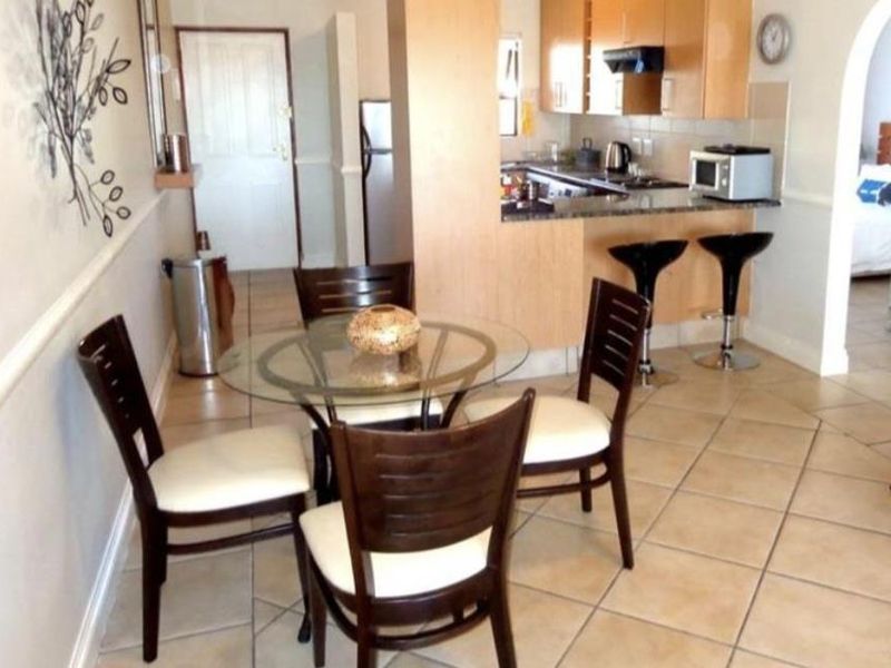 Open plan dining area featuring tiled flooring, seamlessly connected to a functional kitchen with built-in cabinetry, granite countertops, and a breakfast bar.