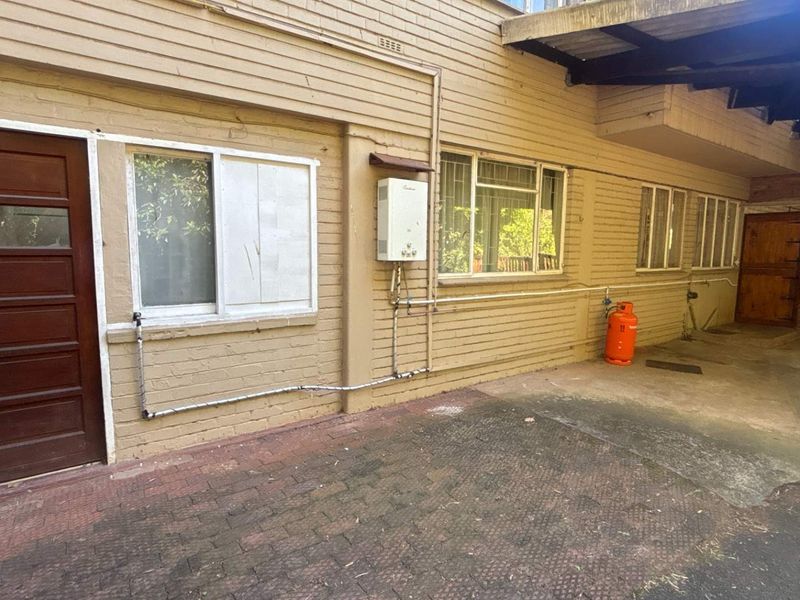 Rear exterior view of the apartment building featuring a paved courtyard, brick facade, and wall-mounted gas water heater.