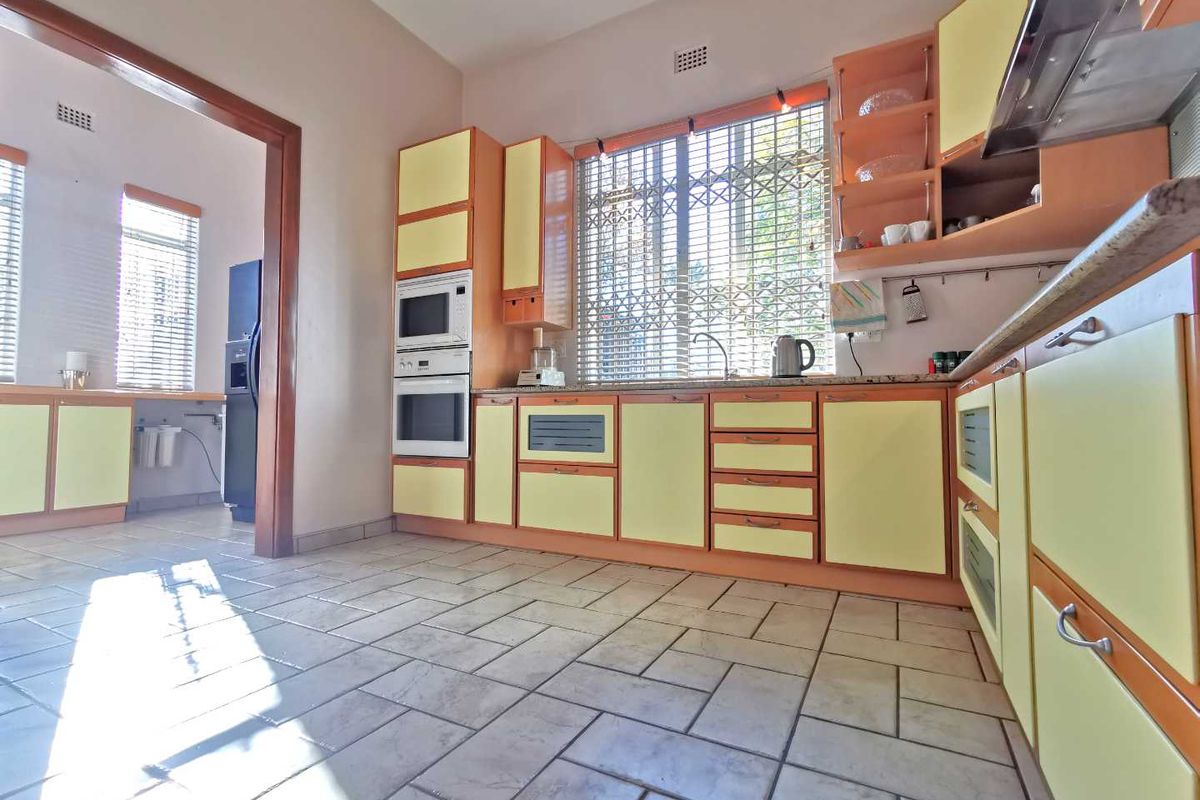 A functional kitchen featuring built-in cabinetry, integrated oven and microwave, stone-look countertops, and tiled flooring, with an adjacent scullery area visible.