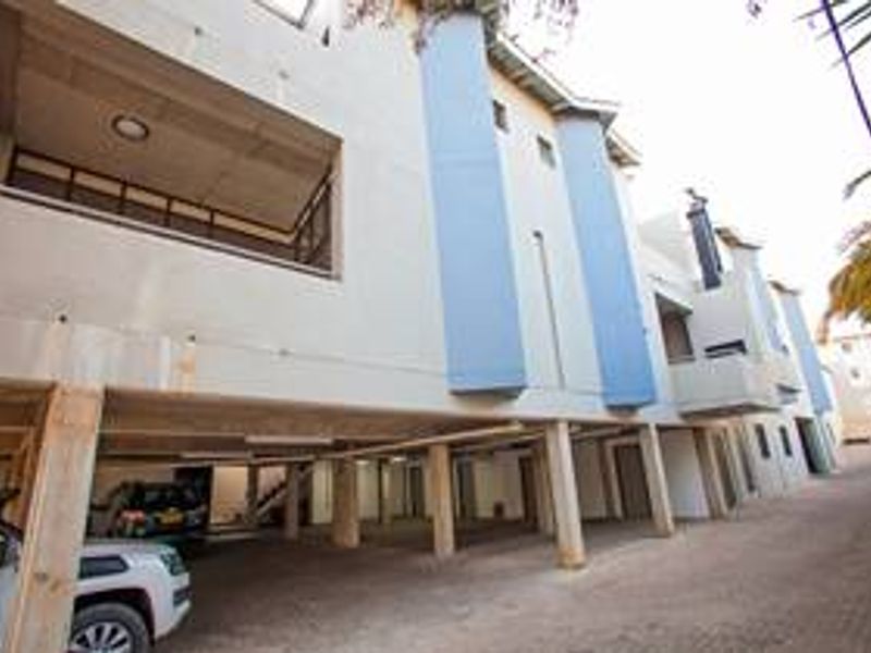 Exterior view of a townhouse complex featuring a covered ground-level parking area with concrete pillars and upper-level balconies.