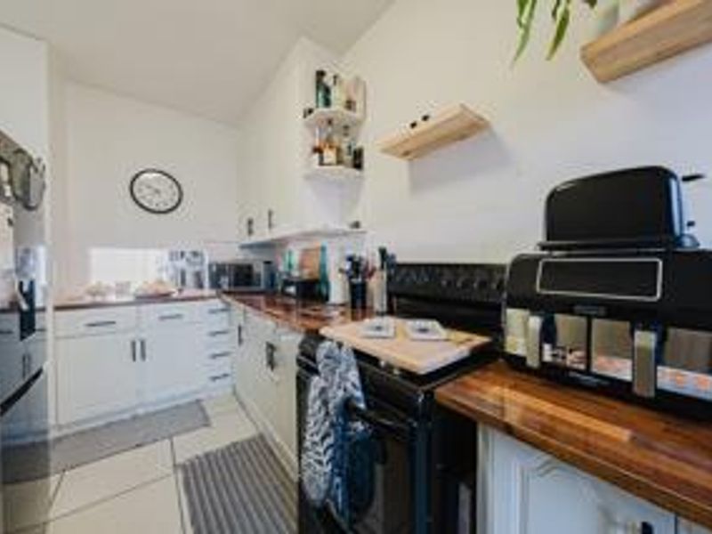 A functional kitchen featuring white cabinetry, warm wooden countertops, and a freestanding oven, providing a practical workspace with tiled flooring.