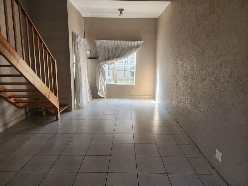 An empty living room featuring ceramic floor tiles, a wooden staircase, and textured walls, offering a blank canvas for interior design.