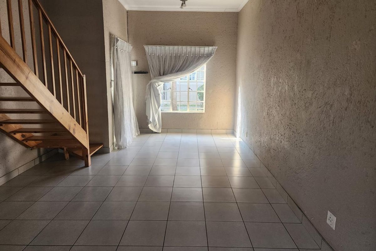 An empty living room featuring ceramic floor tiles, a wooden staircase, and textured walls, offering a blank canvas for interior design.