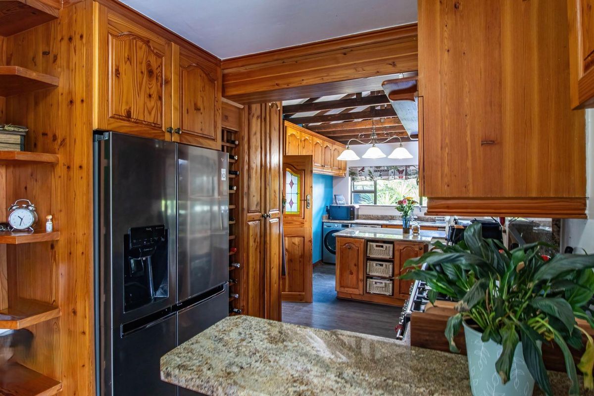 A rustic kitchen featuring extensive timber cabinetry, granite countertops, and an open-plan layout connecting to a secondary prep or laundry area.