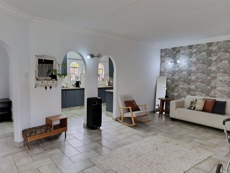 Open plan living area featuring a stone accent wall, tiled flooring, and arched entryways leading into a functional kitchen space.