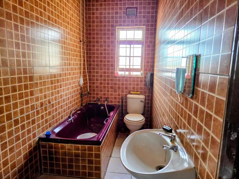 A dated bathroom featuring full-height brown wall tiles, a built-in bathtub, a pedestal basin, and a standard toilet.