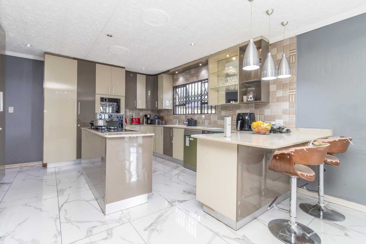 Modern kitchen featuring high-gloss cabinetry, stone countertops, a central island, and marble-look floor tiles, offering a functional and contemporary cooking space.