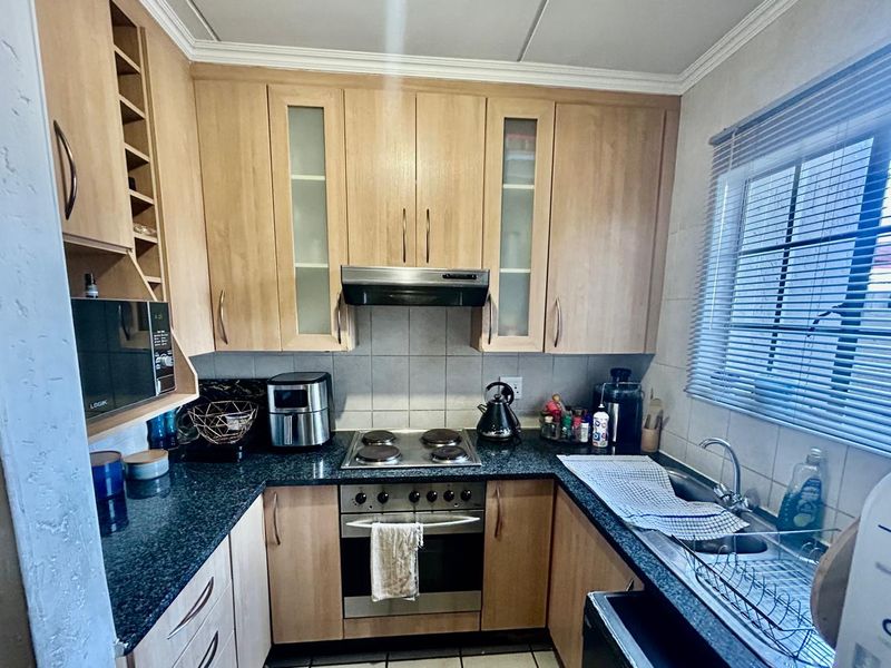 Functional kitchen featuring light wood cabinetry, dark granite countertops, built-in oven, electric hob, and a tiled backsplash with natural light from the window.