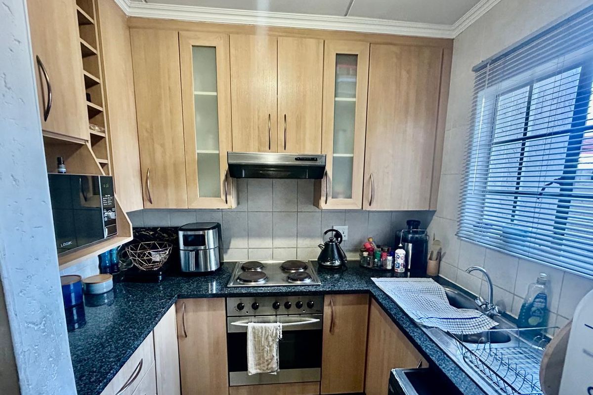 Functional kitchen featuring light wood cabinetry, dark granite countertops, built-in oven, electric hob, and a tiled backsplash with natural light from the window.