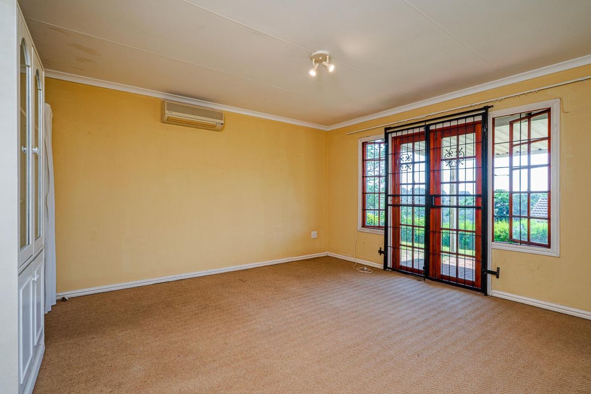 Spacious living room featuring built-in cabinetry, wall-mounted air conditioning unit, and large glass doors with security gates leading to the exterior.