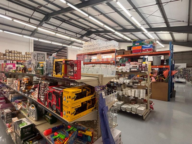 Spacious retail warehouse interior featuring high ceilings with exposed steel trusses, industrial lighting, and durable epoxy flooring with extensive metal shelving infrastructure.