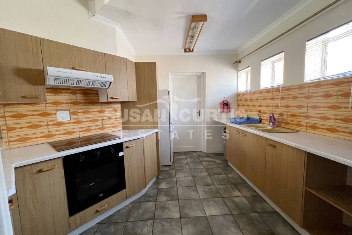 A functional kitchen featuring wood-look cabinetry, laminate countertops, built-in oven and hob, and tiled splashbacks with neutral flooring.