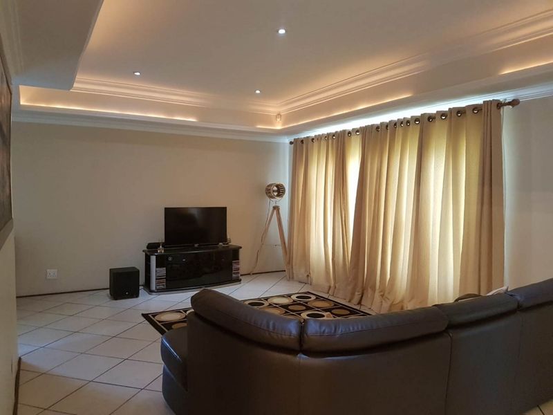 A comfortable living room featuring tiled flooring, a recessed ceiling with integrated cove lighting, and large window treatments.