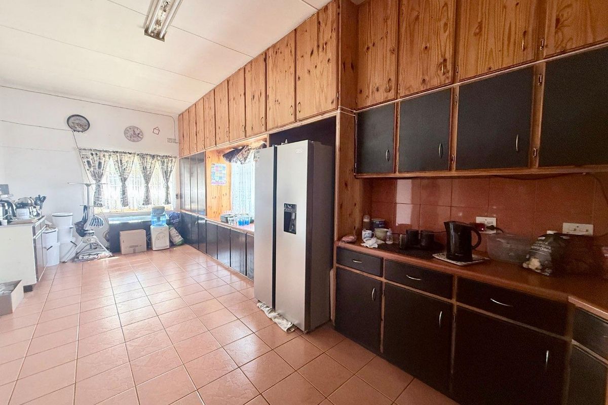 A spacious kitchen featuring extensive built-in wooden cabinetry, tiled flooring, and a tiled splashback, offering significant potential for a modern renovation.