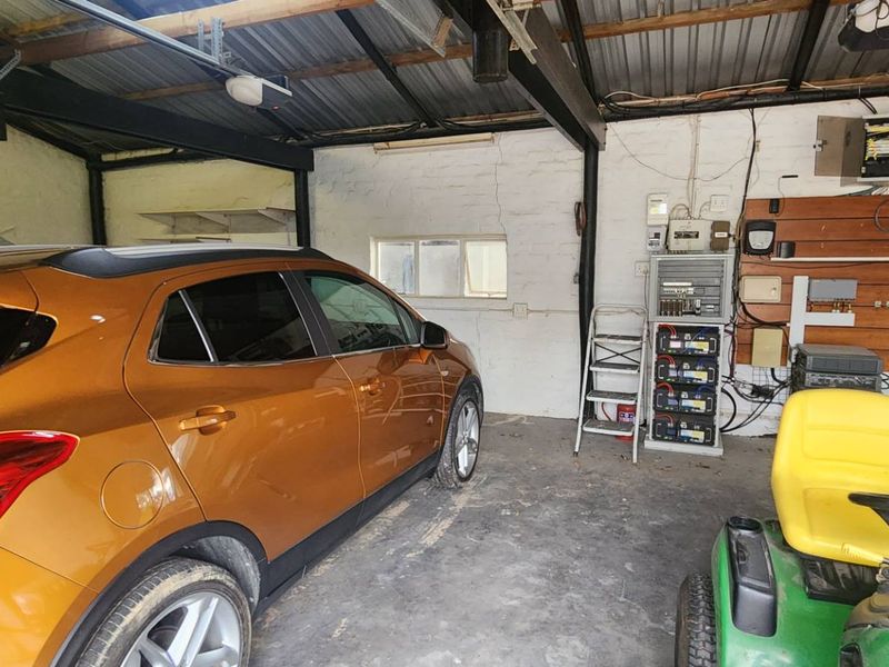 A functional garage space featuring exposed steel beams, corrugated roofing, and a wall-mounted solar power and battery backup system.