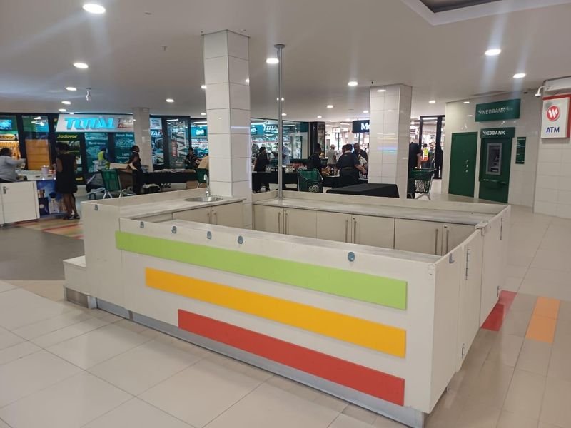 A central retail kiosk unit located within a shopping mall, featuring a built-in counter with an integrated sink and tiled flooring.