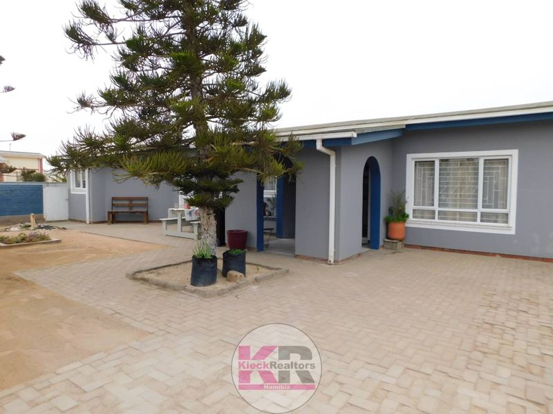 A paved rear courtyard area featuring a mature tree, arched entryway, and security-barred windows on a grey-painted exterior wall.