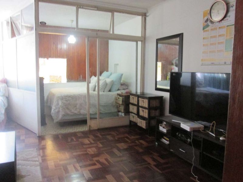 Open plan living area featuring classic parquet flooring and a sliding glass partition separating the bedroom space with timber wall paneling.