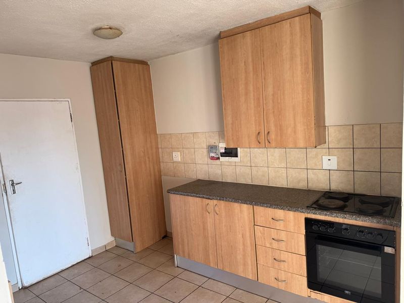 A functional kitchen featuring light wood-look cabinetry, tiled backsplash, and integrated electric oven and hob, offering a clean and practical workspace.